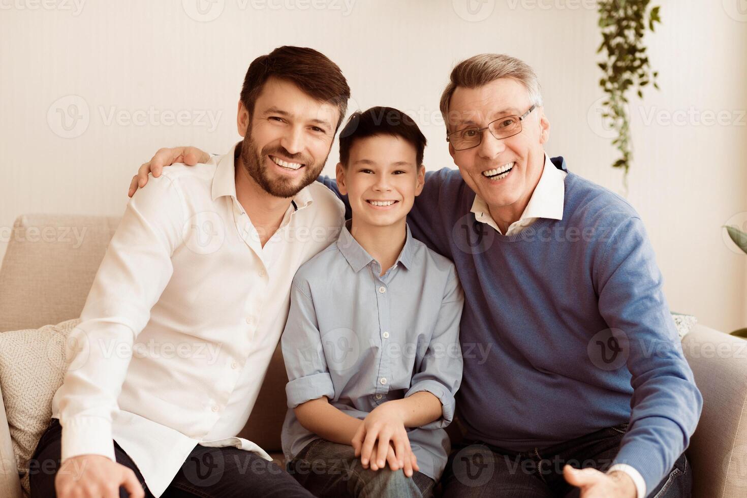 Male Generation. Happy Grandfather With Son And Grandson Smiling At Camera Hugging Sitting Together On Couch At Home. photo