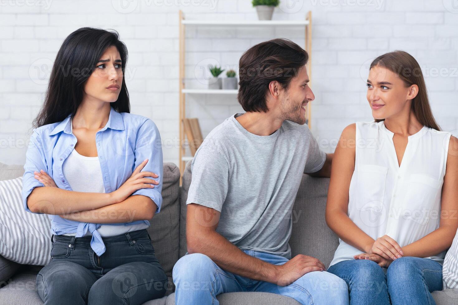 Jealousy And Cheating. Sad Girl Looking At Her Boyfriend Flirting With Another Woman Sitting On Sofa At Home. photo