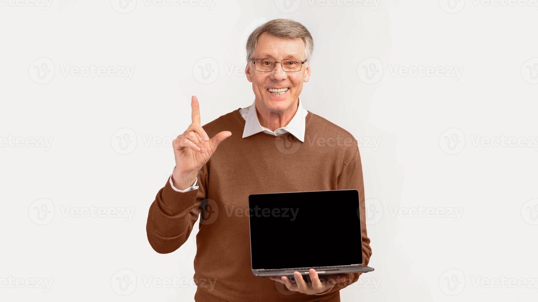 Great Offer. Smiling Senior Man Showing Laptop Blank Screen Pointing Finger Up Standing On White Studio Background. Panorama, Empty Space photo