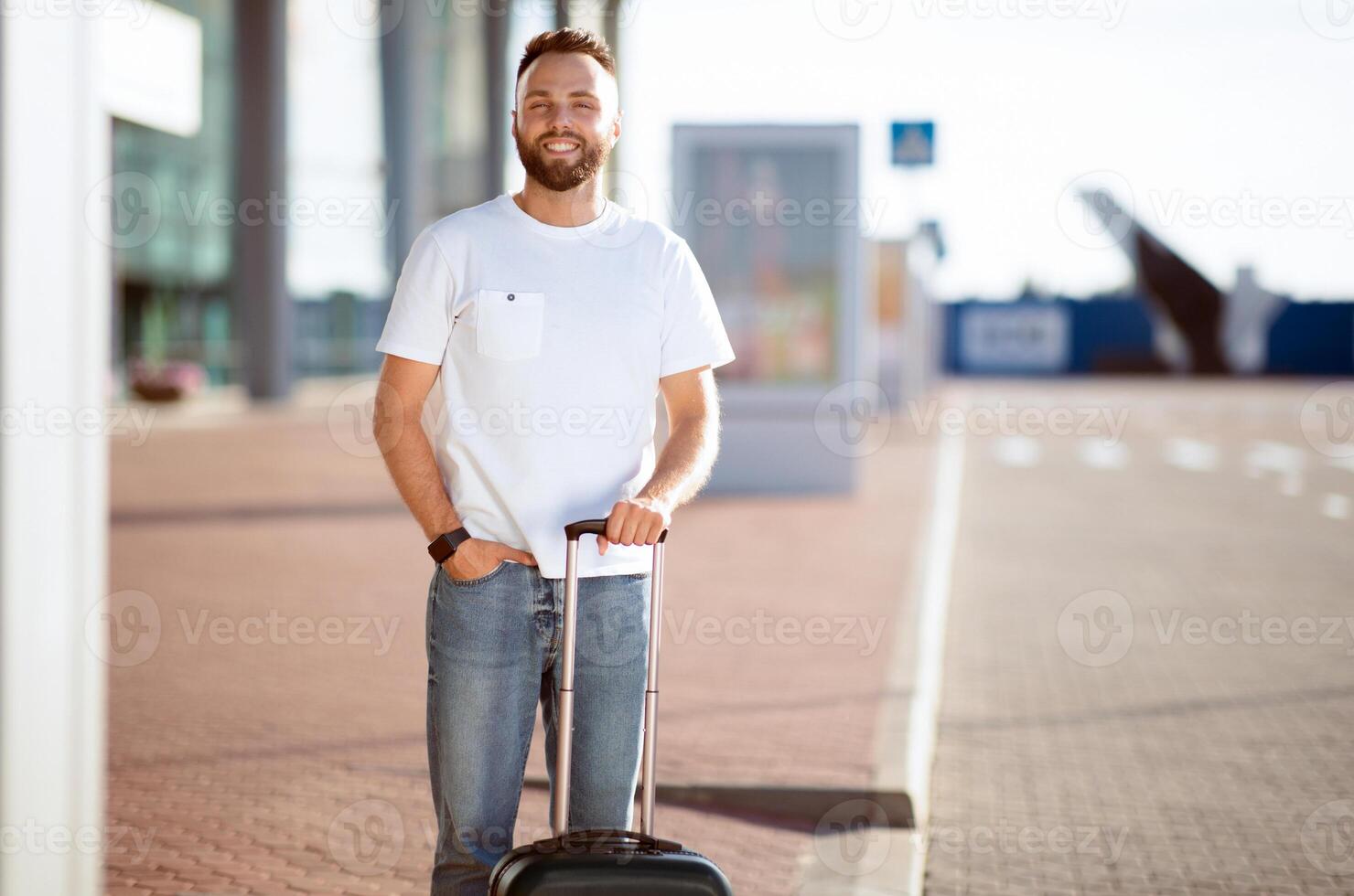 Summer Vacation Concept. Smiling uy standing with baggage near airport terminal, ready for a trip, front view photo