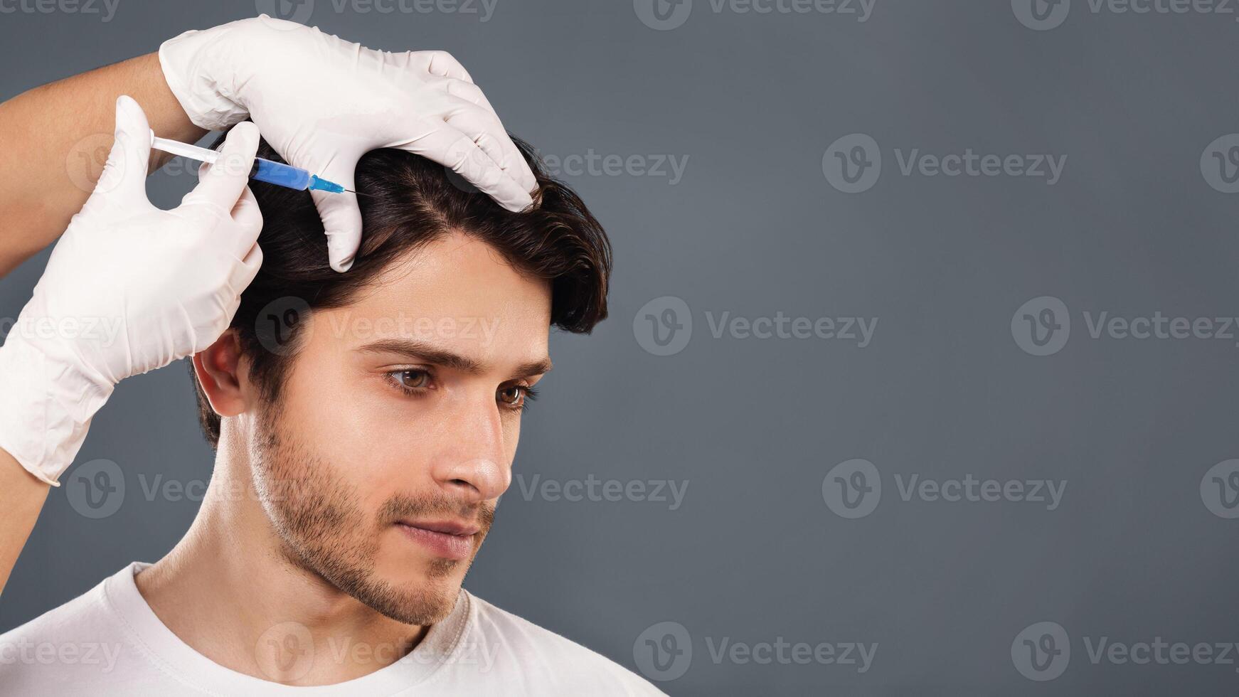 Man with hair loss problem receiving injection in head, grey background, empty space photo