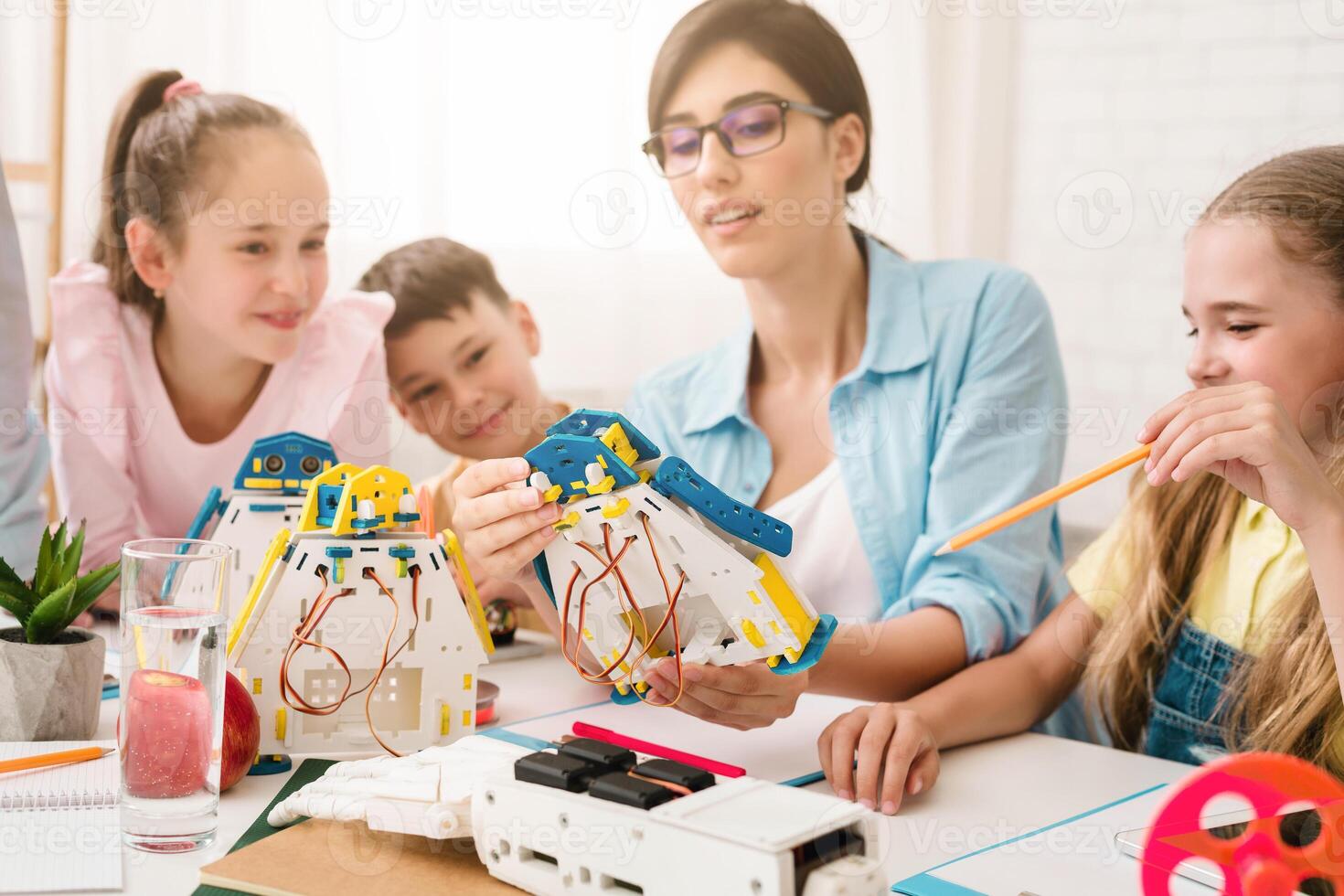 A group of young students are learning about robotics and engineering in a classroom setting. A teacher is helping them build and program a robot, while they work together and ask questions. photo