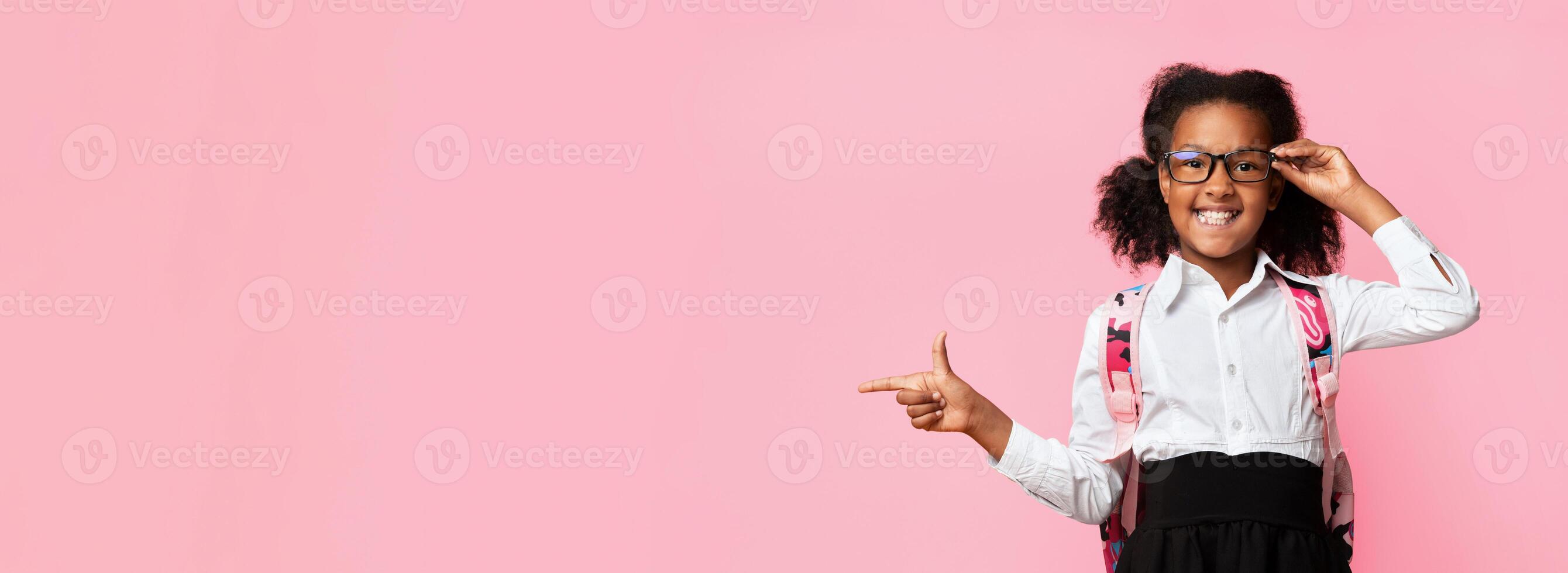 African American Schoolgirl Pointing Finger Aside At Free Space Recommending Something Over Yellow Studio Background. Panorama photo