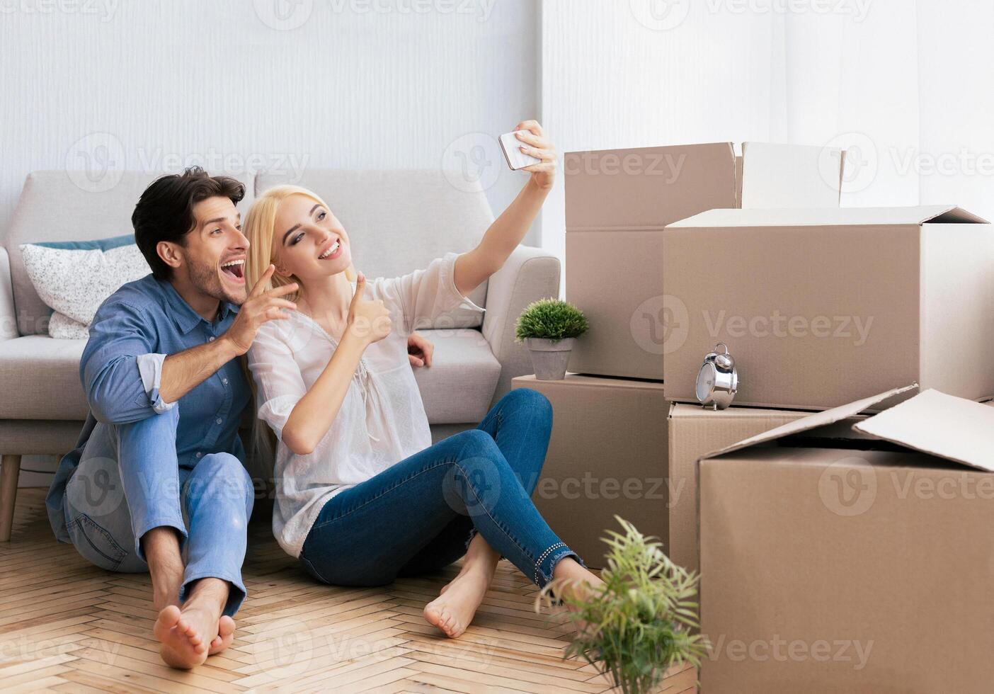 A couple smiles for a selfie as they sit among moving boxes in their new home. photo