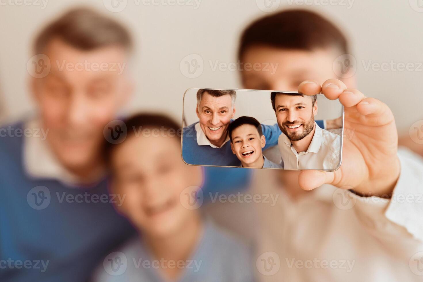 Three Generations Family Selfie. Man, His Son And Elderly Father Taking Picture Of Themselves On Smartphone Sitting Together Indoor photo