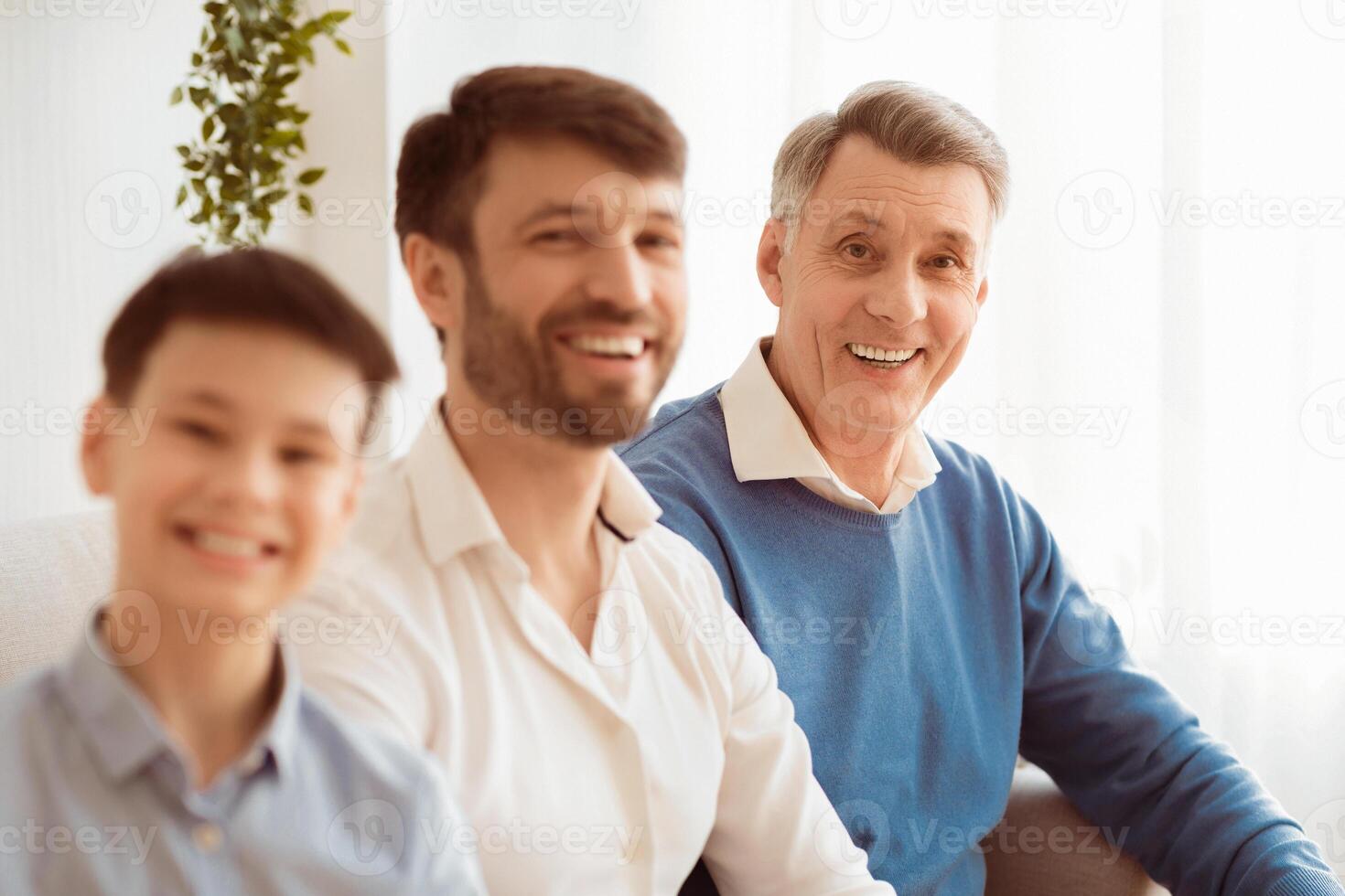 Happy Elderly Man With Middle-Aged Son And Grandson Smiling At Camera Sitting On Couch At Home. Selective Focus photo