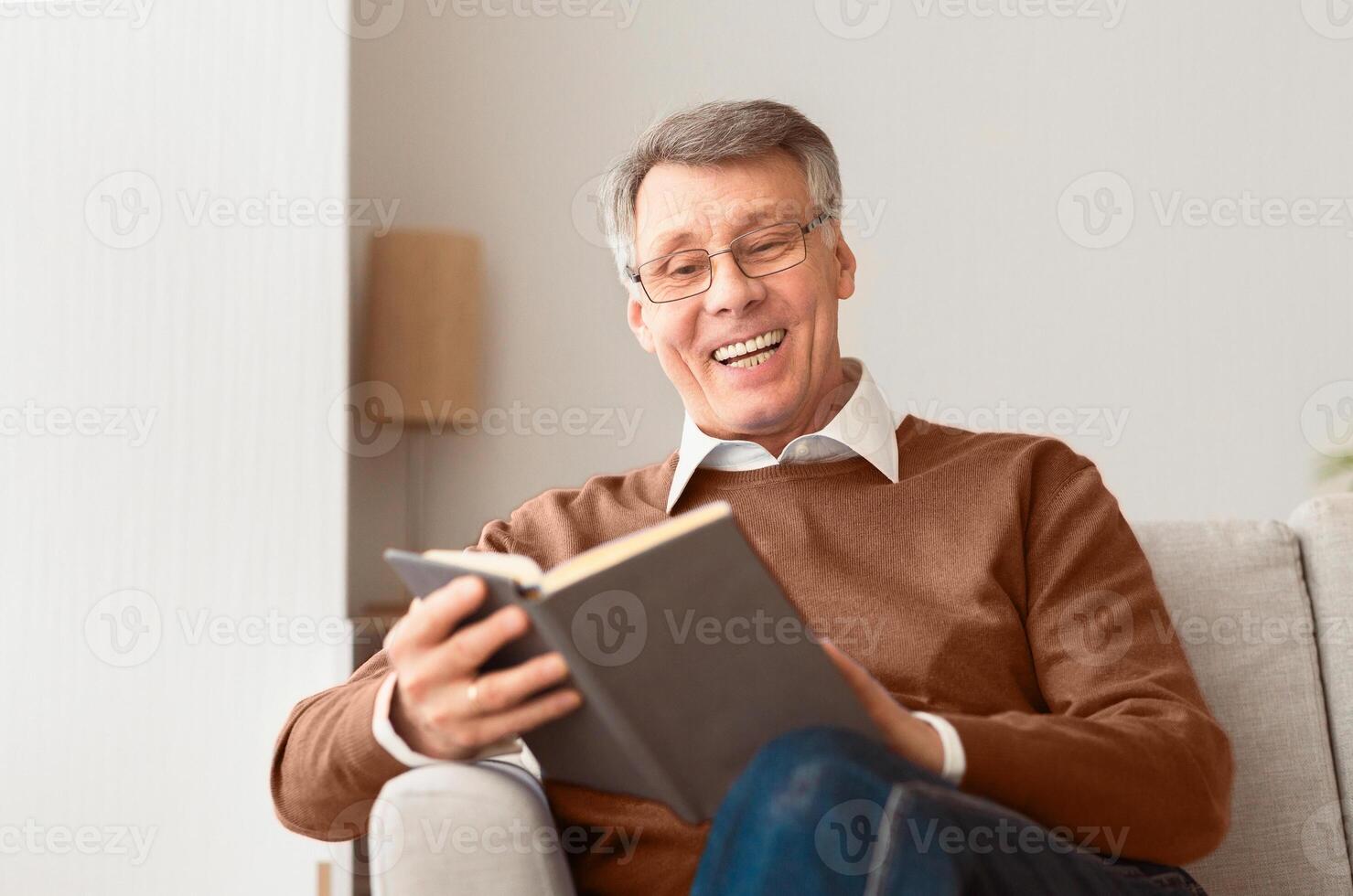 Happy Retirement. Senior Man Reading Book Relaxing Sitting On Sofa At Home. Selective Focus photo