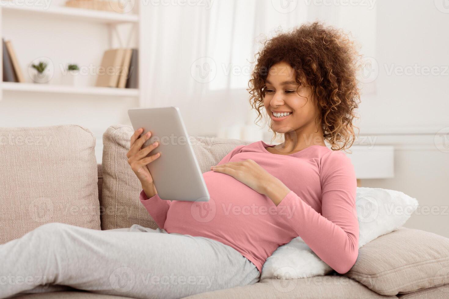 Order kids clothes. Happy pregnant girl using tablet, browsing internet at home photo