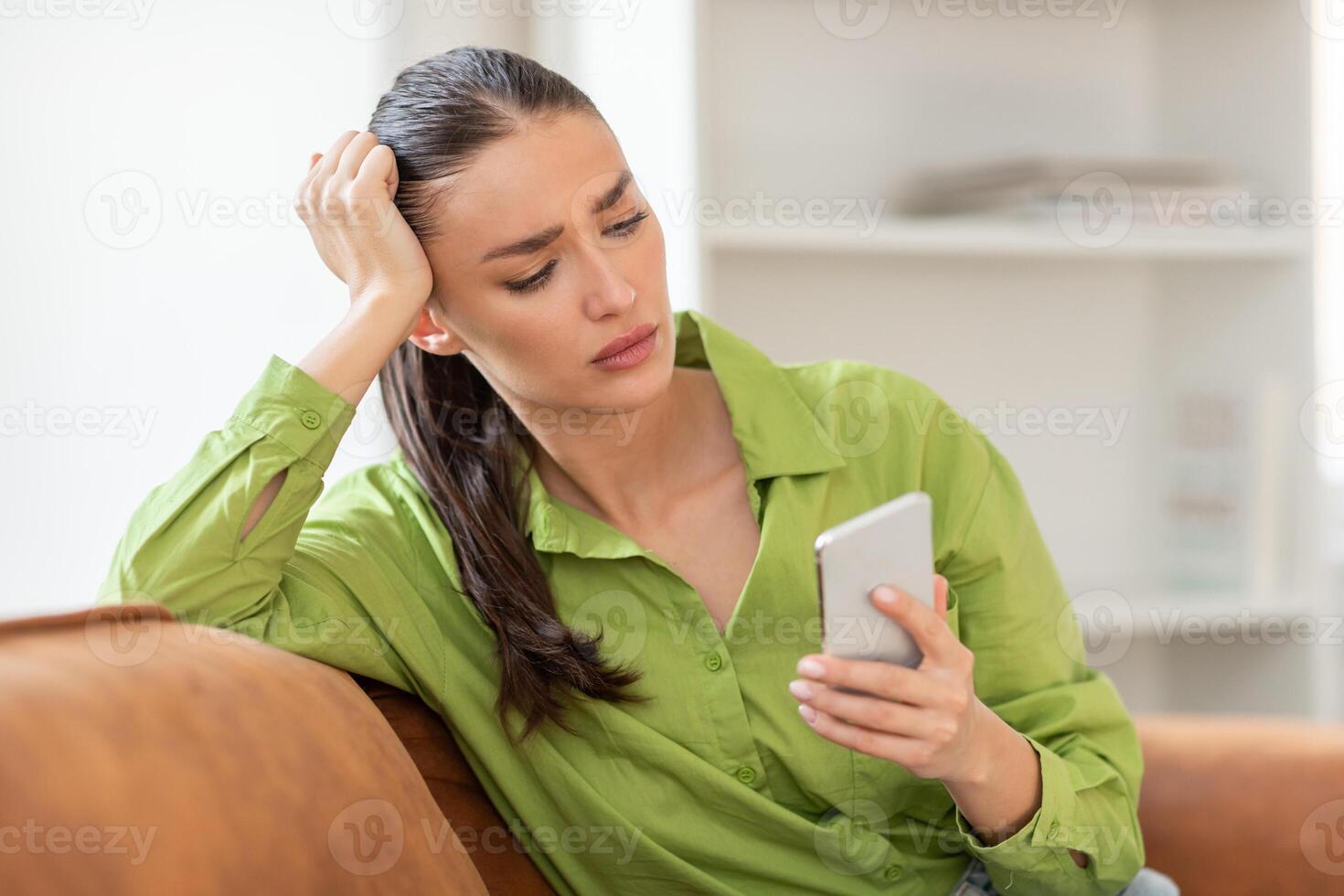 A woman sitting on a couch indoors, engrossed in her cell phone screen. She appears focused as she scrolls and interacts with the device, seemingly unaware of her surroundings. photo