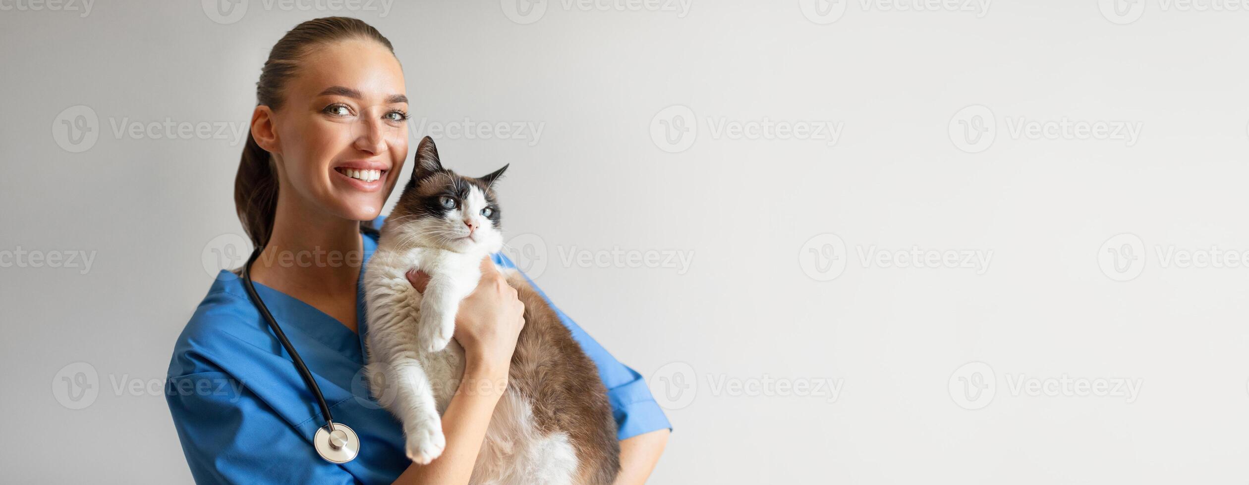 Portrait Of Happy Veterinarian Doctor Woman Holding A Cat, Posing With Healthy Feline Patient Over Gray Studio Background, Smiling At Camera. Pet Health Care And Routine Check Up Concept, Copy Space photo