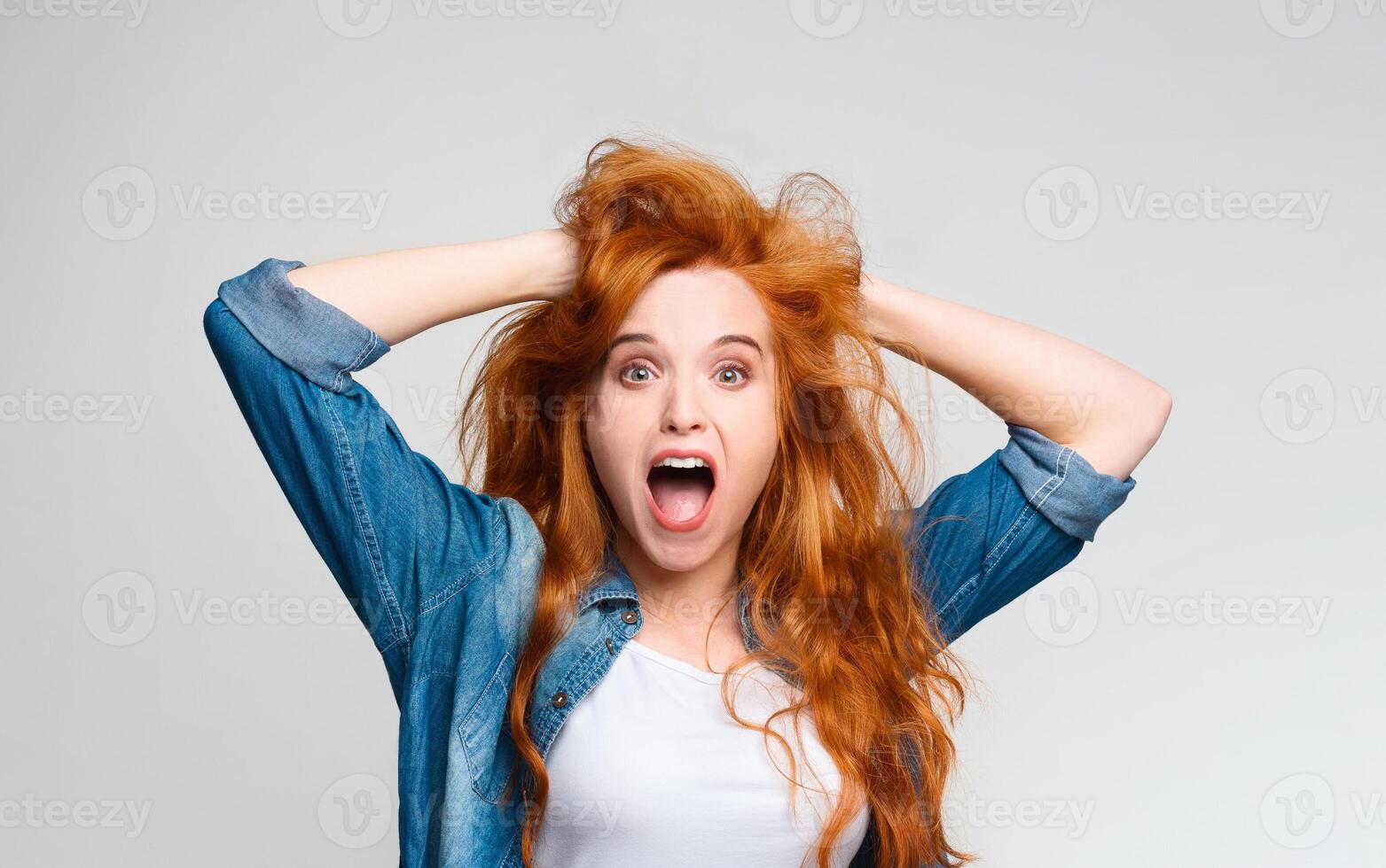 Unbelievable amazing news. Millennial redhead woman clutched her head in shock and surprise, screaming at camera photo