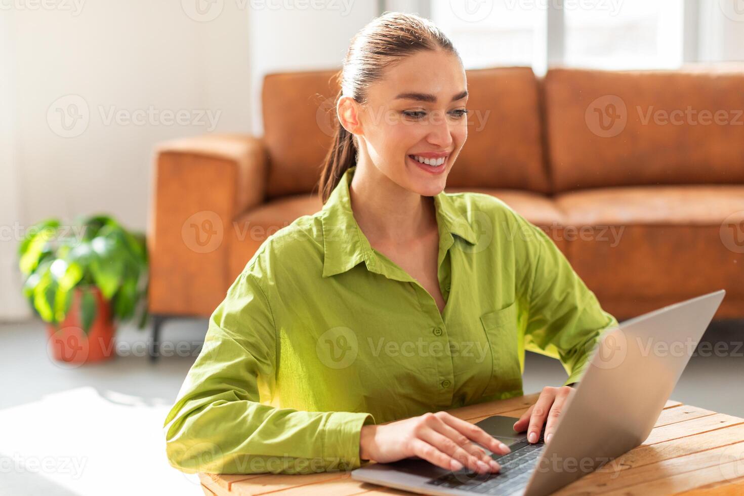 A woman is seated at a table, concentrating on her laptop computer. She is typing on the keyboard and looking at the screen intently, focused on her work. photo