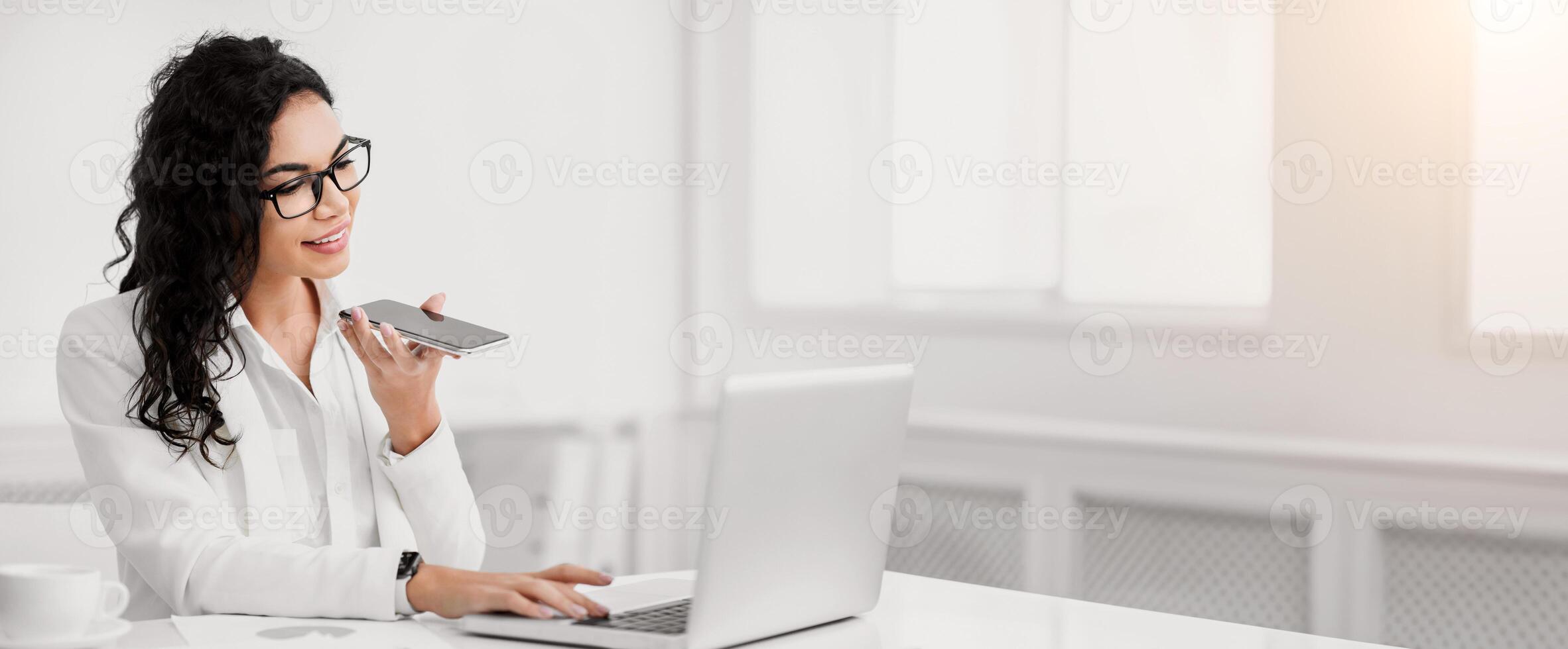 Voice Search. Smiling latin woman using smart phone voice recognition to send message at workplace, copyspace photo