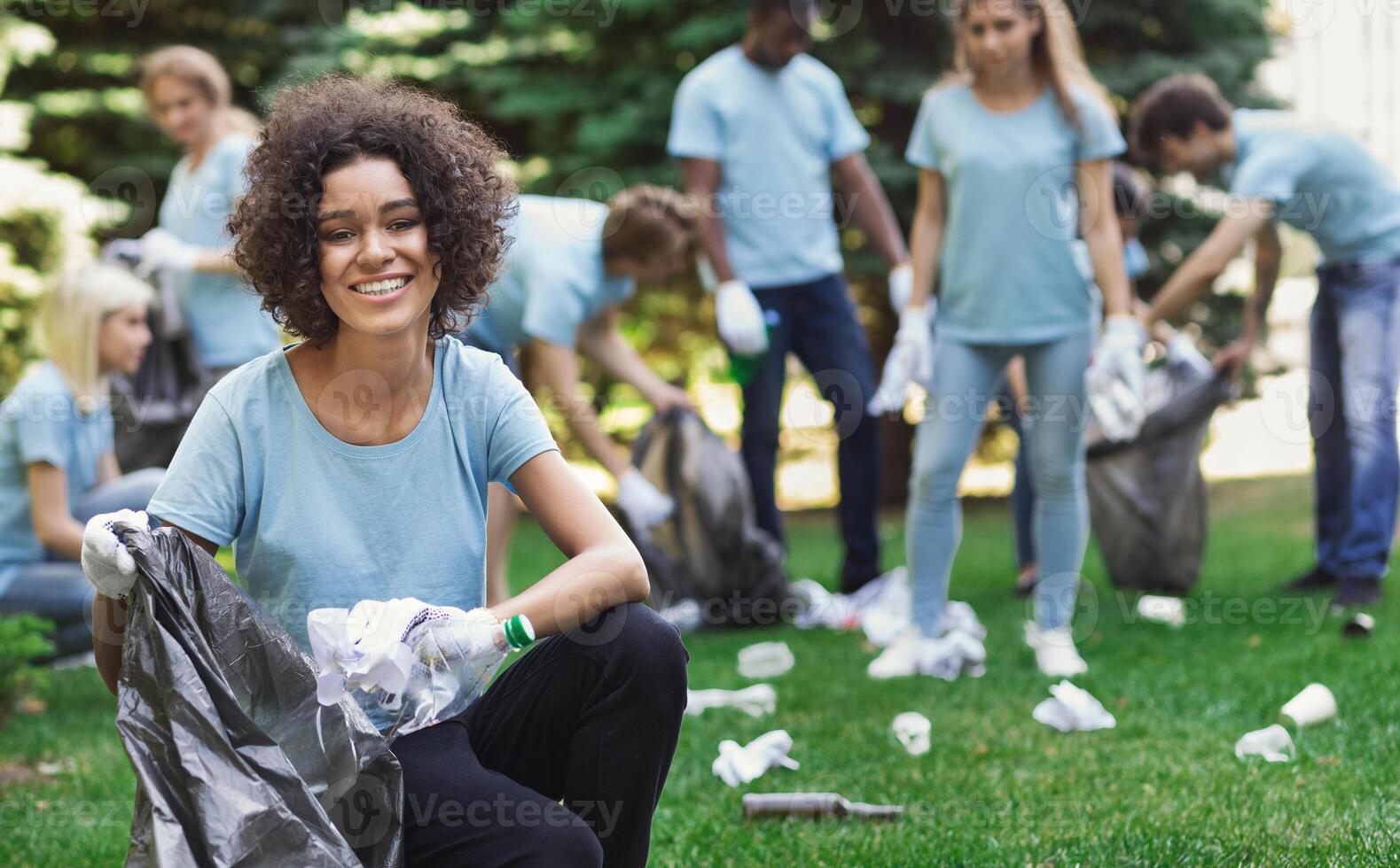 Volunteering, charity and clean environment concept. Happy black woman and group of volunteers with garbage bags cleaning area in park, copy space photo