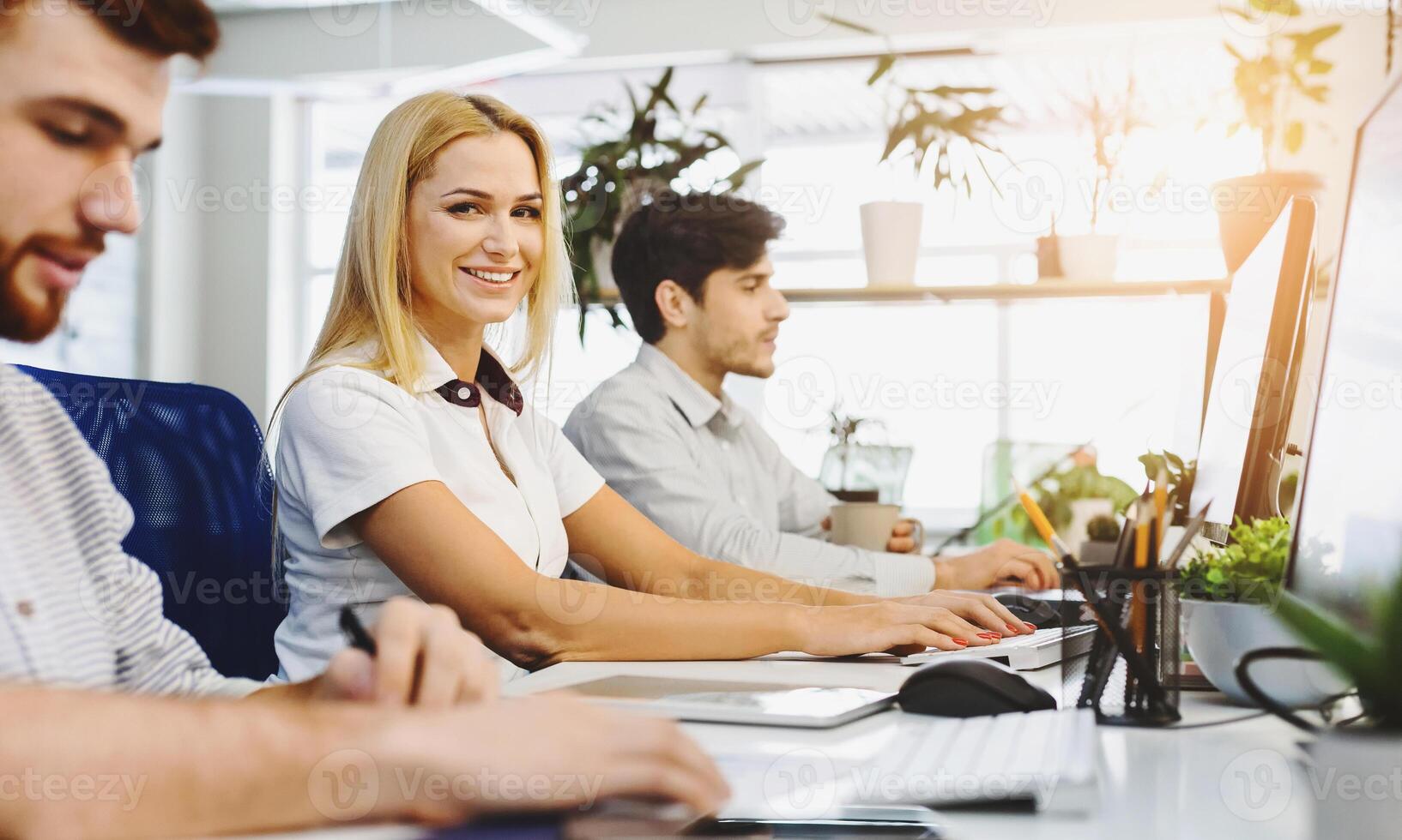 A group of diverse individuals are sitting at a desk, concentrating intently as they work on their computers. Each person is focused on their screen, typing, clicking, and scrolling photo