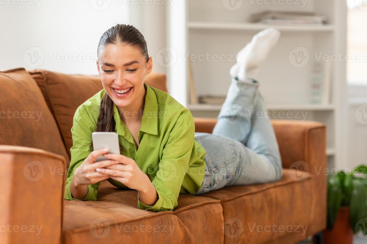 A woman is laying down on a couch while using a cell phone. She appears relaxed and focused on the screen as she interacts with the device. photo