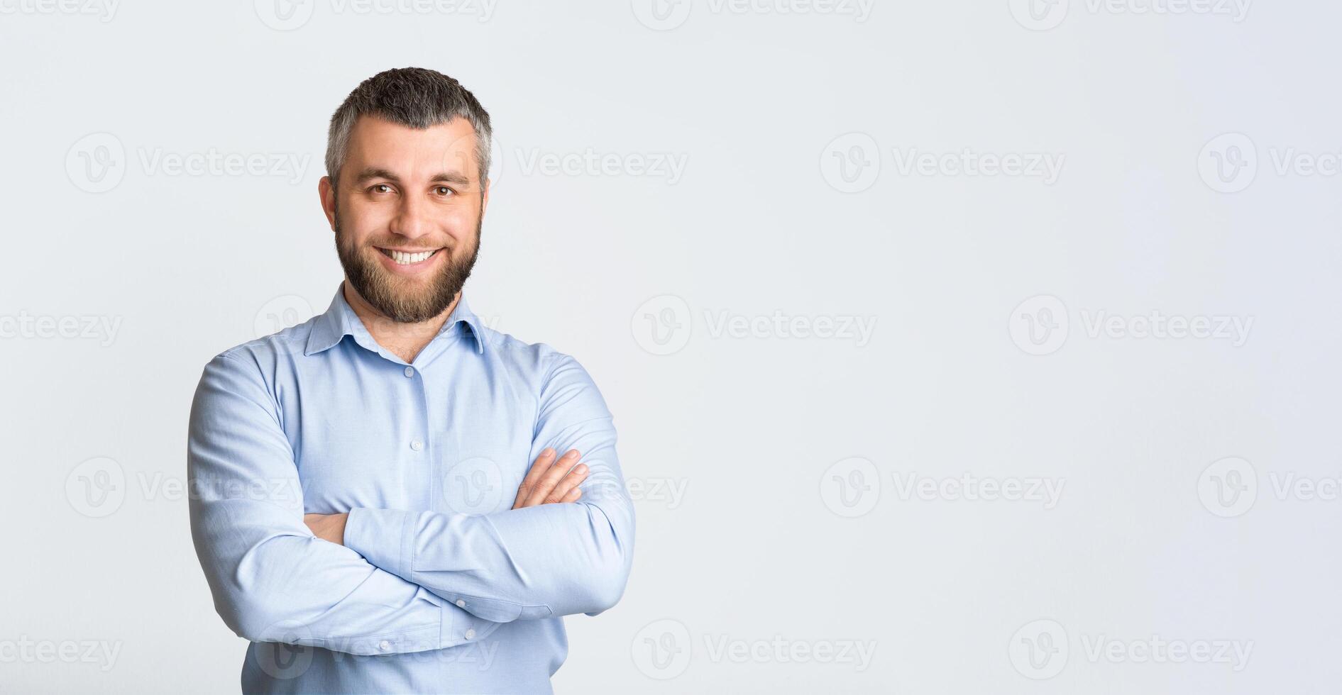 A man wearing a blue shirt is confidently posing for a picture, standing in a relaxed manner, smiling towards the camera. He appears to be enjoying the moment and is striking a casual pose, panorama photo