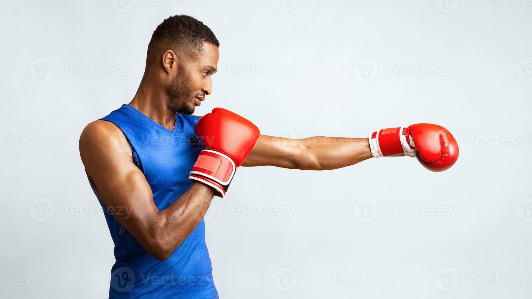 Ultimate Workout. Side view portrait of focused afro guy in red boxing gloves doing punch isolated on yellow studio wall photo