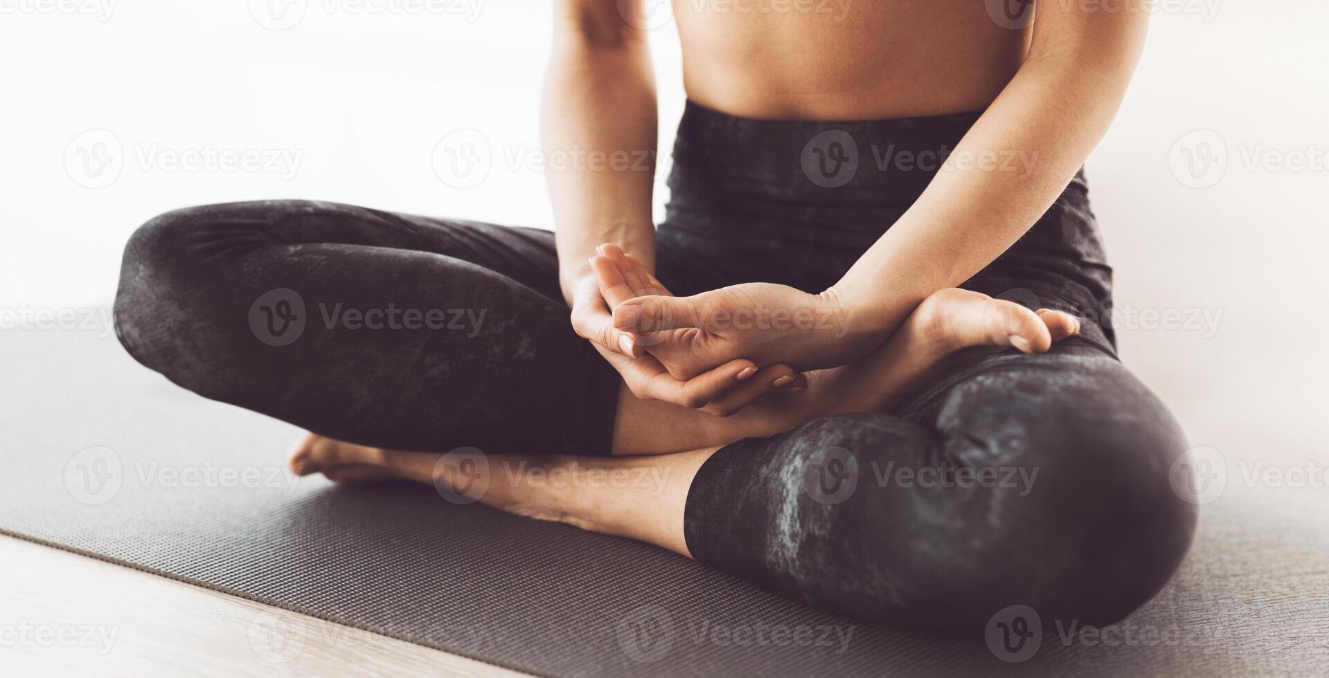 Cropped of flexible woman is engrossed in a session of yoga, demonstrating an advanced seated pose with precise hand placement on a mat. photo