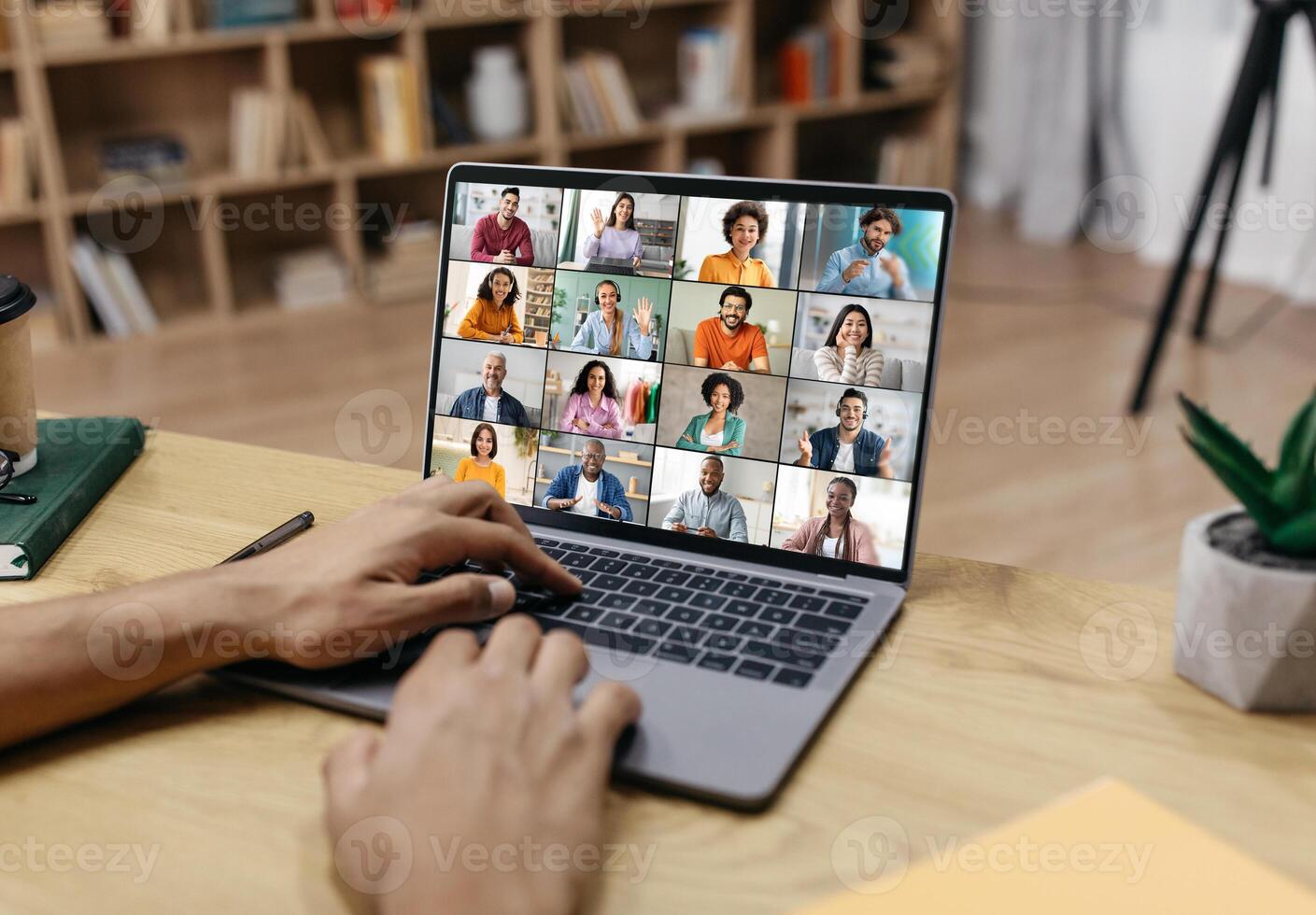 A persons hands are shown typing on a laptop keyboard, the screen of which displays a conference with multiple participants. photo