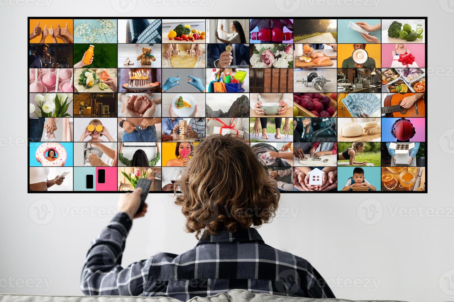 A man sits on a couch, facing a television screen, watching a montage of images. The screen is filled with a grid of various pictures, each depicting a different scene or activity. photo
