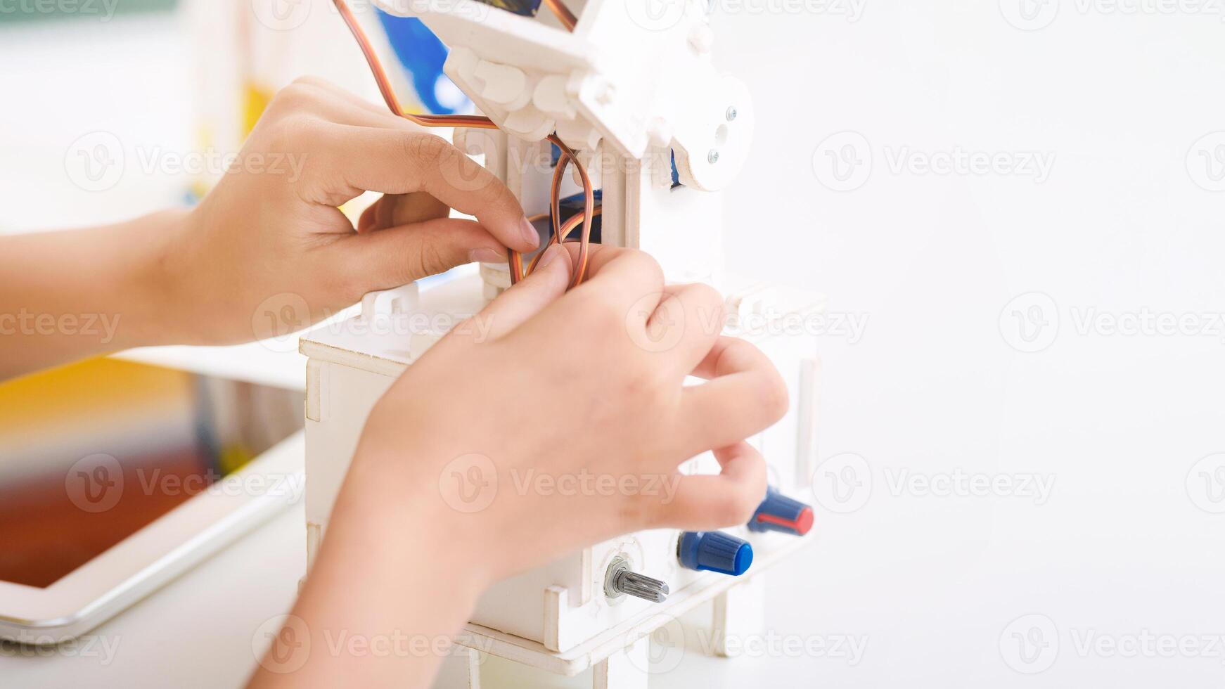 A close-up image of two hands working on a robotic toy kit, the hands are gently attaching a small copper wire to the robots assembly, copy space photo