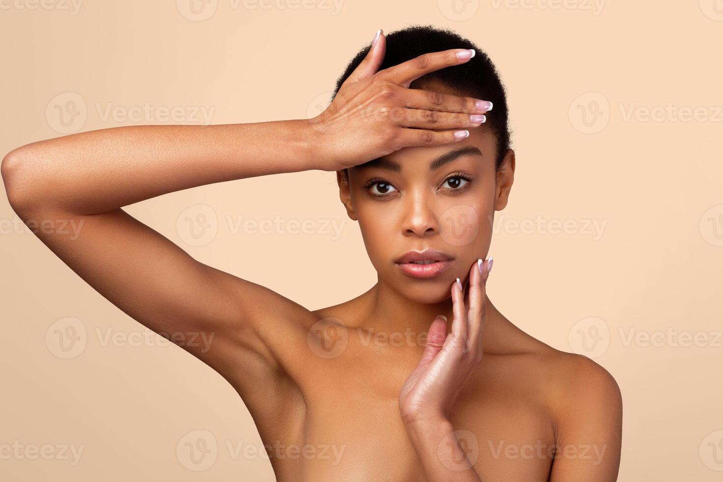 Portrait Of Sensual Black Lady Posing Touching Perfect Face Looking At Camera Standing Shirtless Over Gray Background. Studio Shot. Facial Skincare And Beauty Treatment Concept photo
