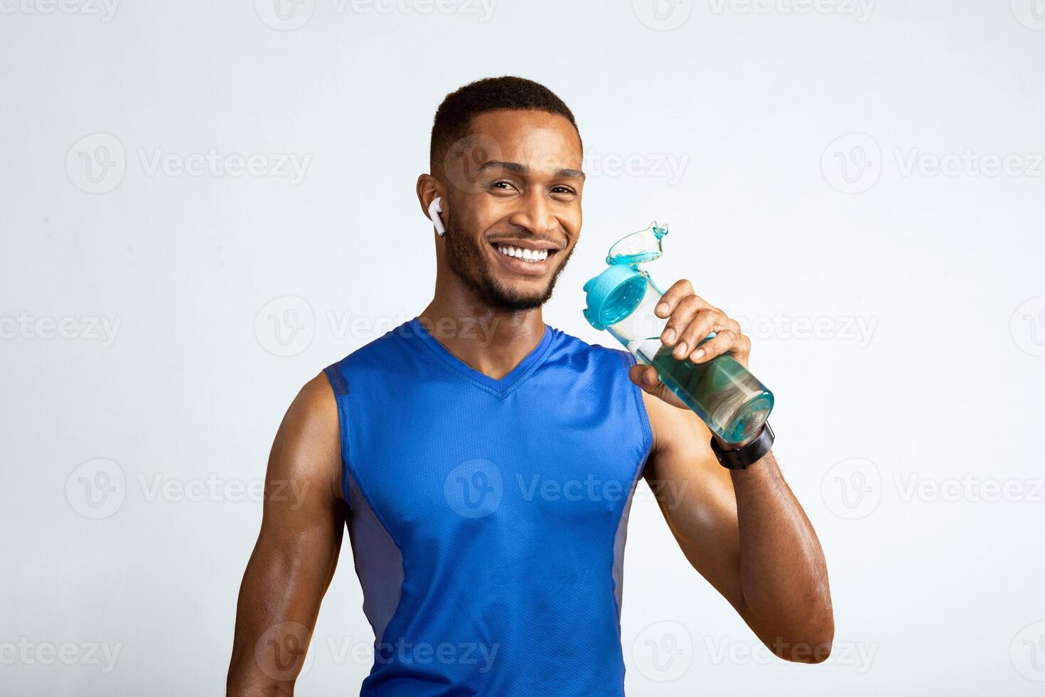 Marathon Runner. Happy afro guy in earbuds drinking water from bottle, yellow studio background, copyspace photo