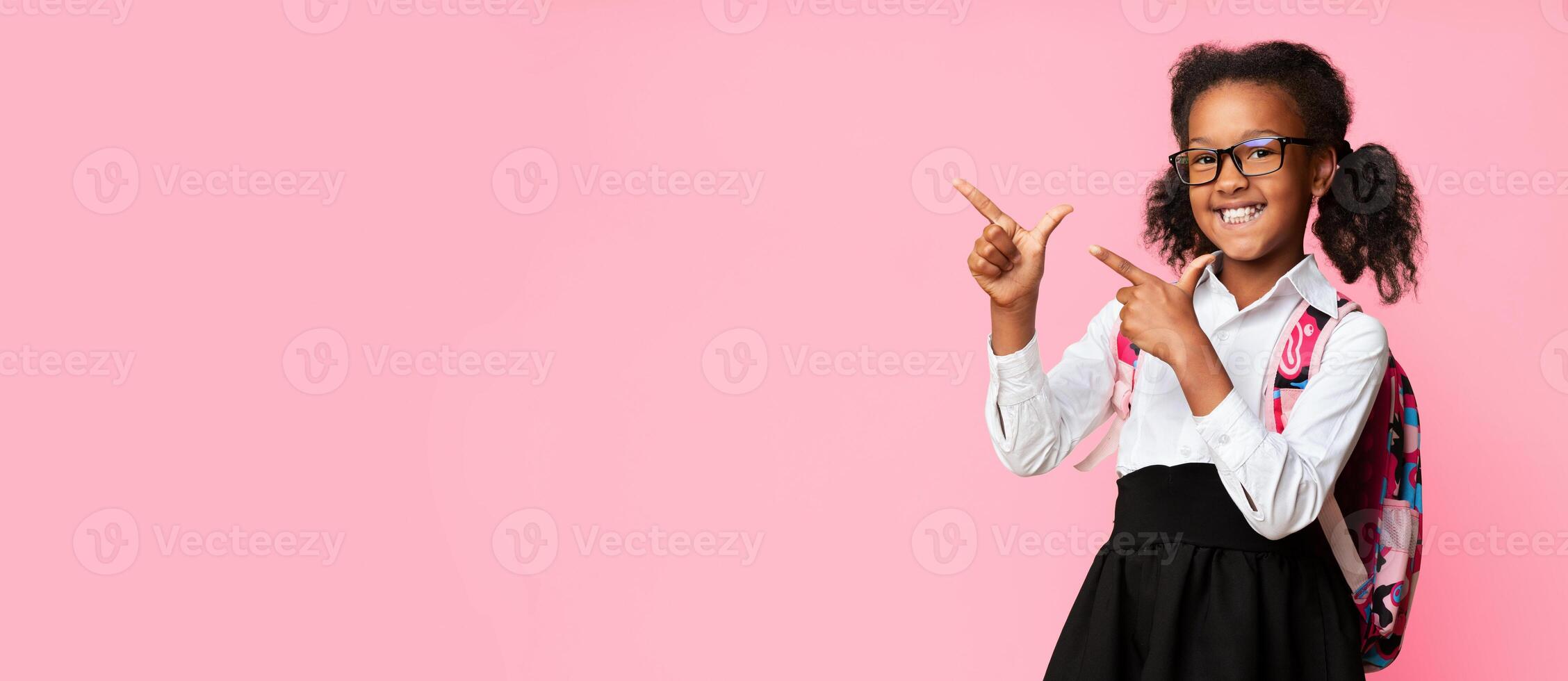 Cheerful Black Schoolgirl Pointing Fingers At Copy Space Recommending Distant Online Classes Over Yellow Background. Panorama photo