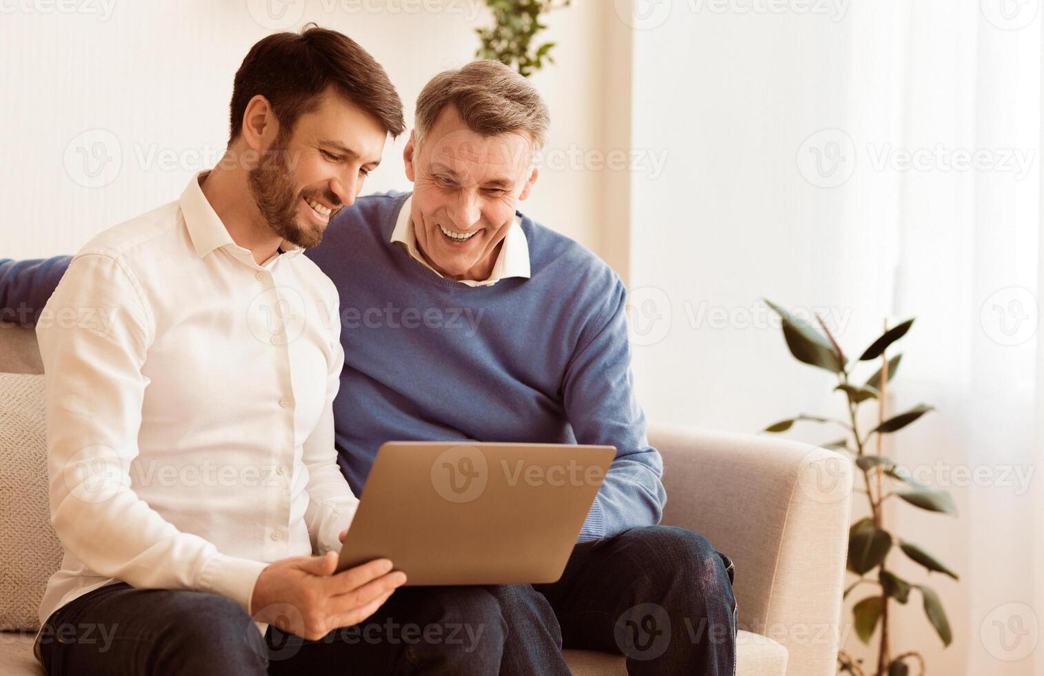 Happy Mature Son And Senior Father Using Laptop Sitting On Sofa At Home. Free Space, Selective Focus photo