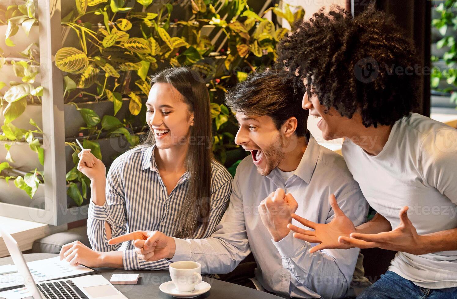 Happy young entrepreneurs at cafe celebrating success or starting new project, looking at laptop together and shouting, empty space photo