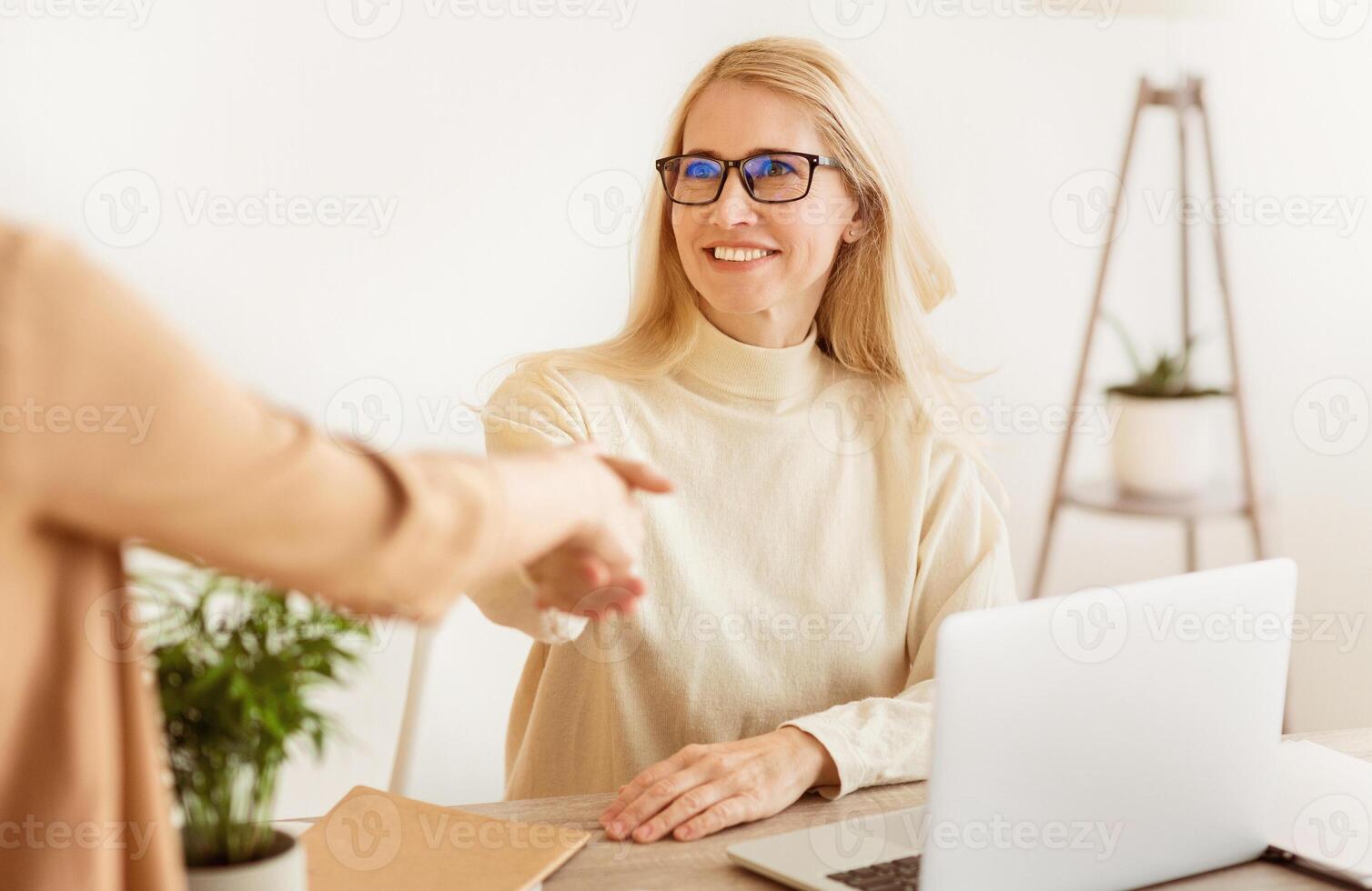 A businesswoman in glasses smiles and shakes hands with a colleague in a professional office setting. photo