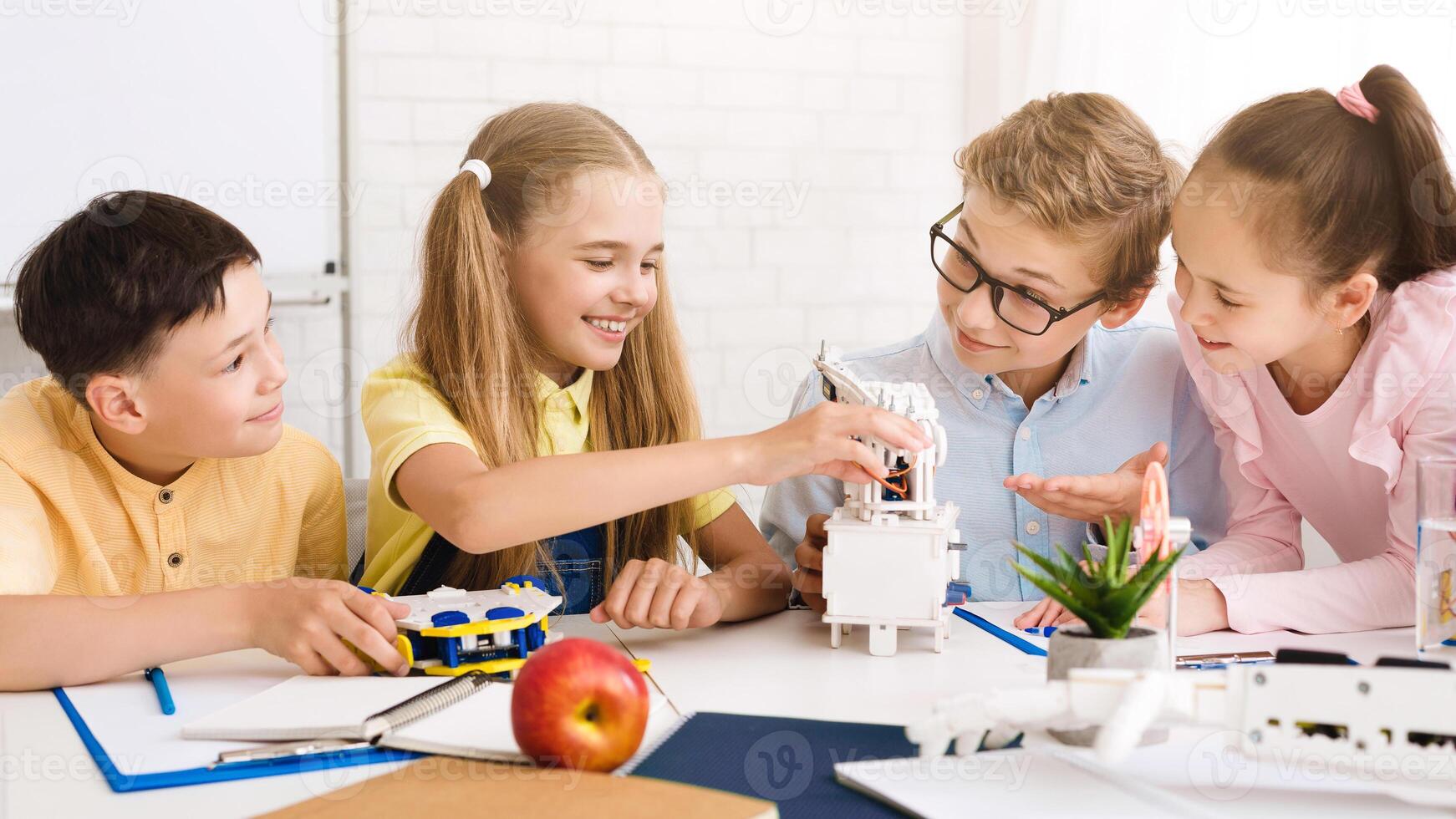 Four children, two boys and two girls, are working together on a robotics project in a classroom setting. They are all smiling and appear to be engaged in the task at hand photo