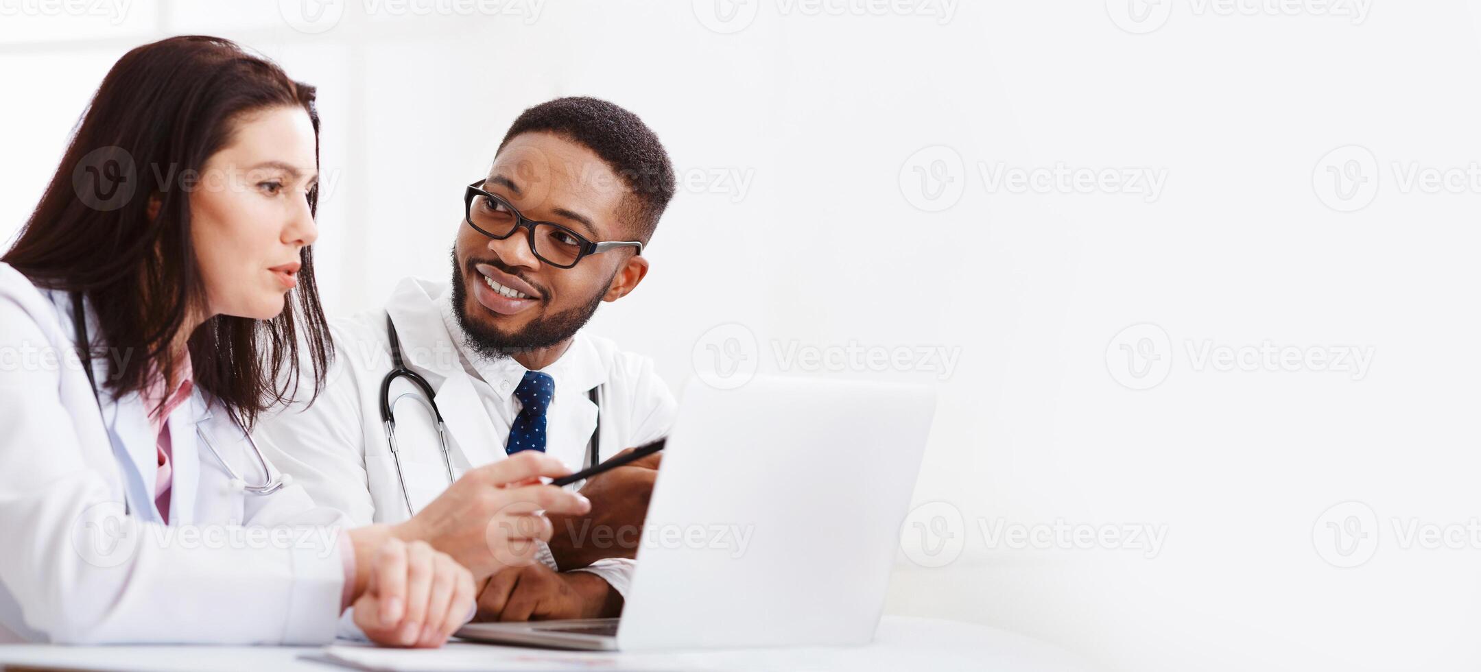 Two Medical Doctors Consulting, Using Laptop And Discussing Diagnosis Questions In Office photo