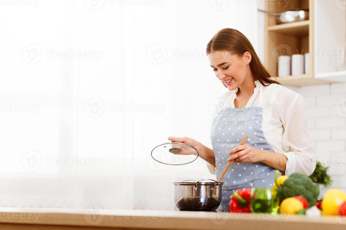Millennial Woman Cooking In Kitchen, Stiring Soup With Wooden Spoon, Copy Space photo