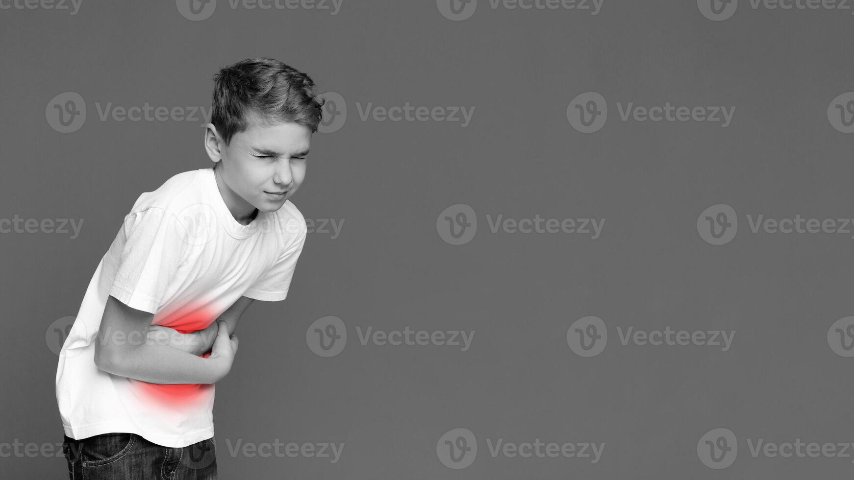 An image of a youngster visibly in discomfort, clutching his stomach, depicted in pain on an isolated grey background photo