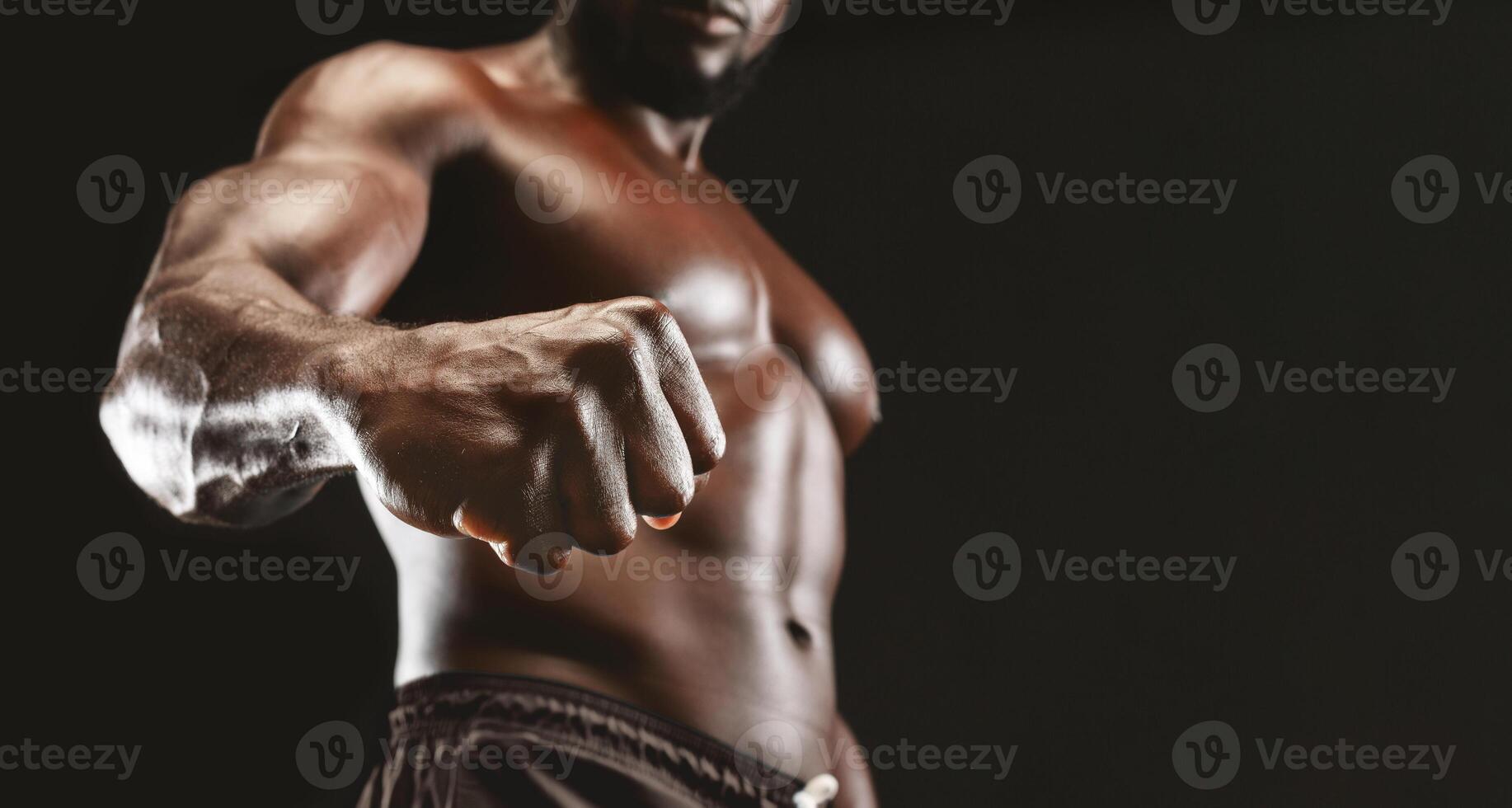 Male power. Confident muscular black guy showing strong fist to camera, panorama photo