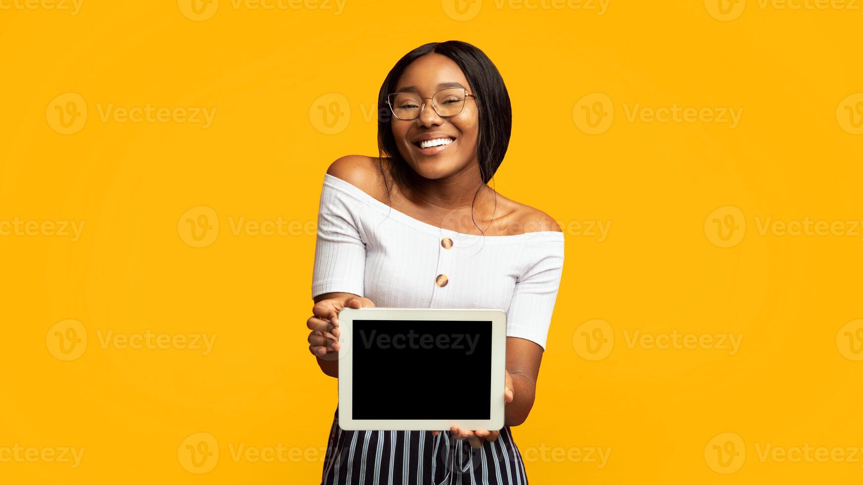 Great Application. Smiling Afro Girl Showing Digital Tablet With Blank Screen Standing In Studio Over Orange Background. Panorama, Mockup photo