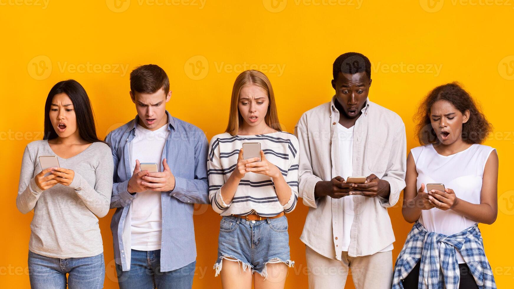 Problematic smartphone use. Multiracial group of teenagers using mobile phones over yellow background, panorama photo
