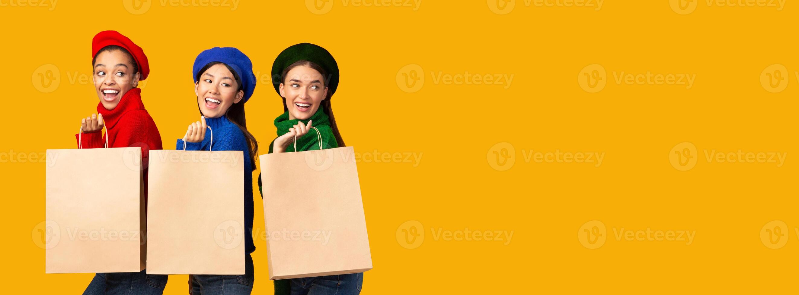 Three Happy Girls On Shopping Holding Paper Shopper Bags Standing Over Yellow Background In Studio. Mockup, Panorama photo