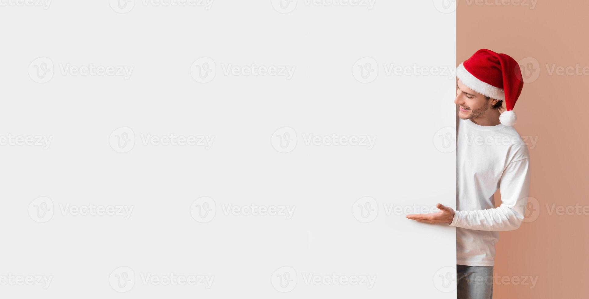 Cheerful Interracial Couple In Santa Hats Pointing At White Billboard With Free Space For Advertisement Or Text, Yellow Background photo
