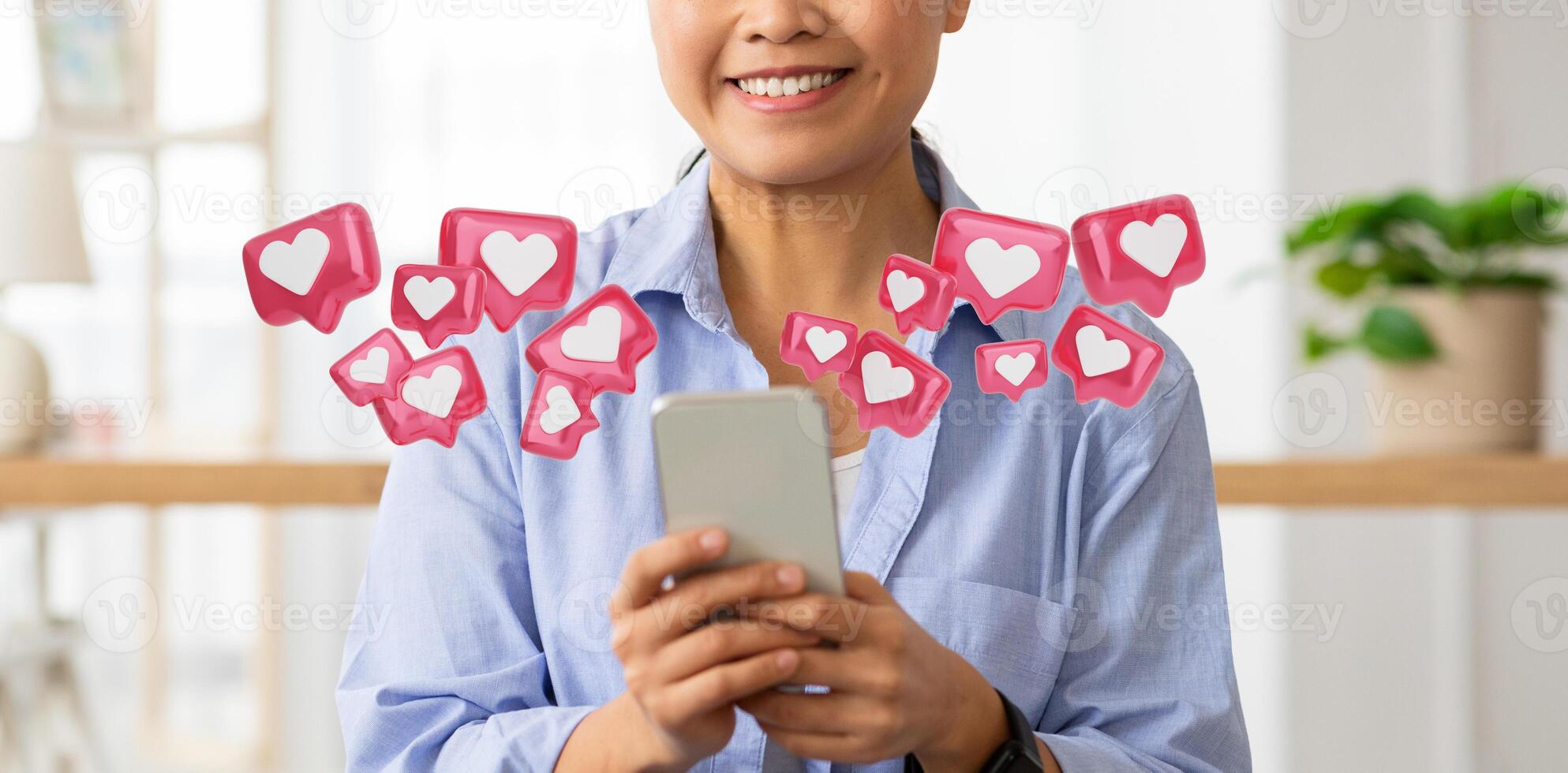 A woman is smiling while looking at her smartphone. The screen is not visible, but there are numerous heart shaped icons floating around her, suggesting she is receiving positive feedback, cropped photo