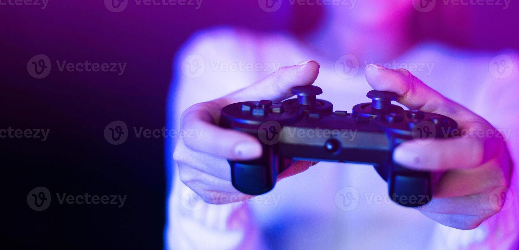 A woman is seen holding a game controller in front of a vibrant purple light, engaged in a gaming session. The controller is illuminated by the vivid purple glow, creating a striking contrast. photo