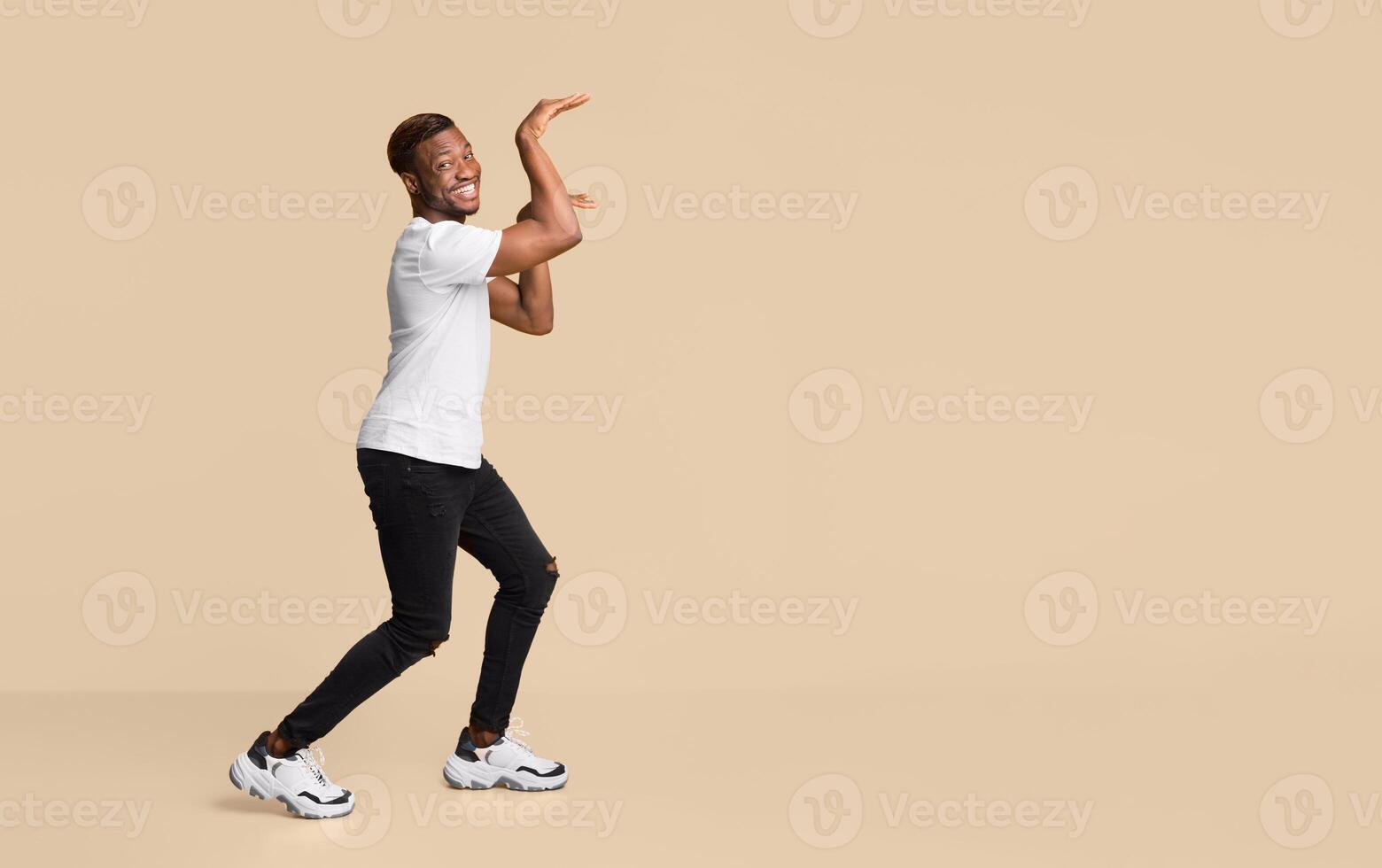 Funny Black Guy Dancing In Egypt Style Having Fun And Fooling Over Orange Studio Background. Free Space For Text photo