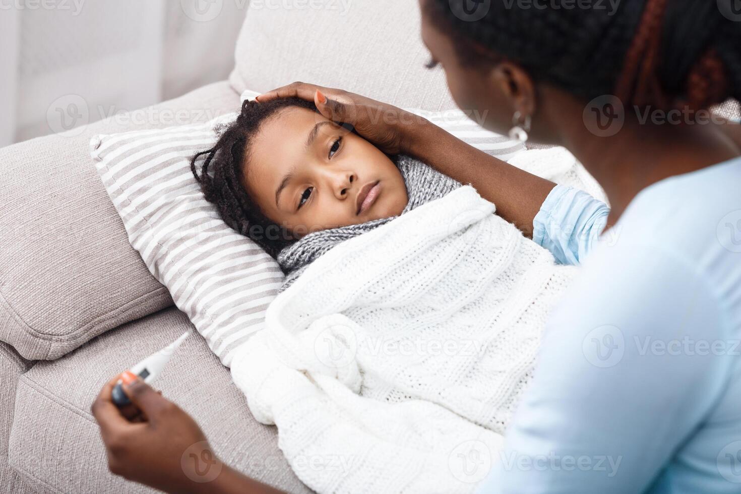 Fever Concept. Sick child in bed, mother holding thermometer, comforting poor girl photo