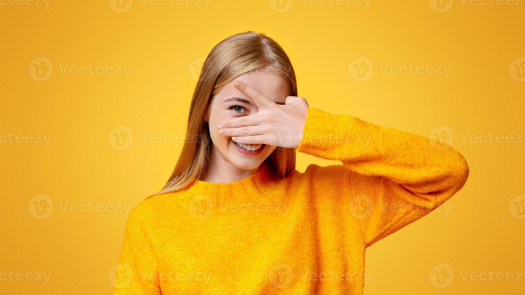 Playful teen girl covering face with hand and peeking through fingers over orange background with copy space photo