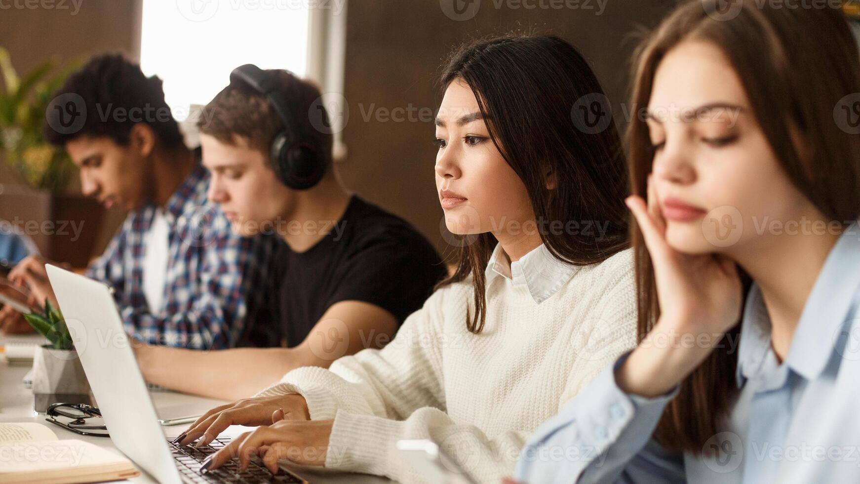 Diverse students sitting at college library, making notes, using laptop and doing homework photo