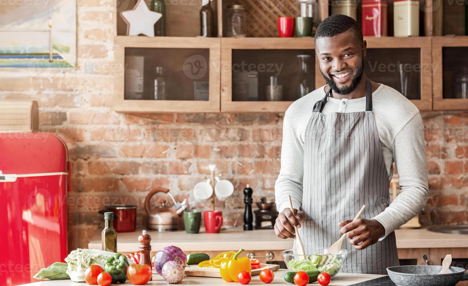 Smiling african man preparing fresh healthy salad at kitchen, cooking for family, copy space photo