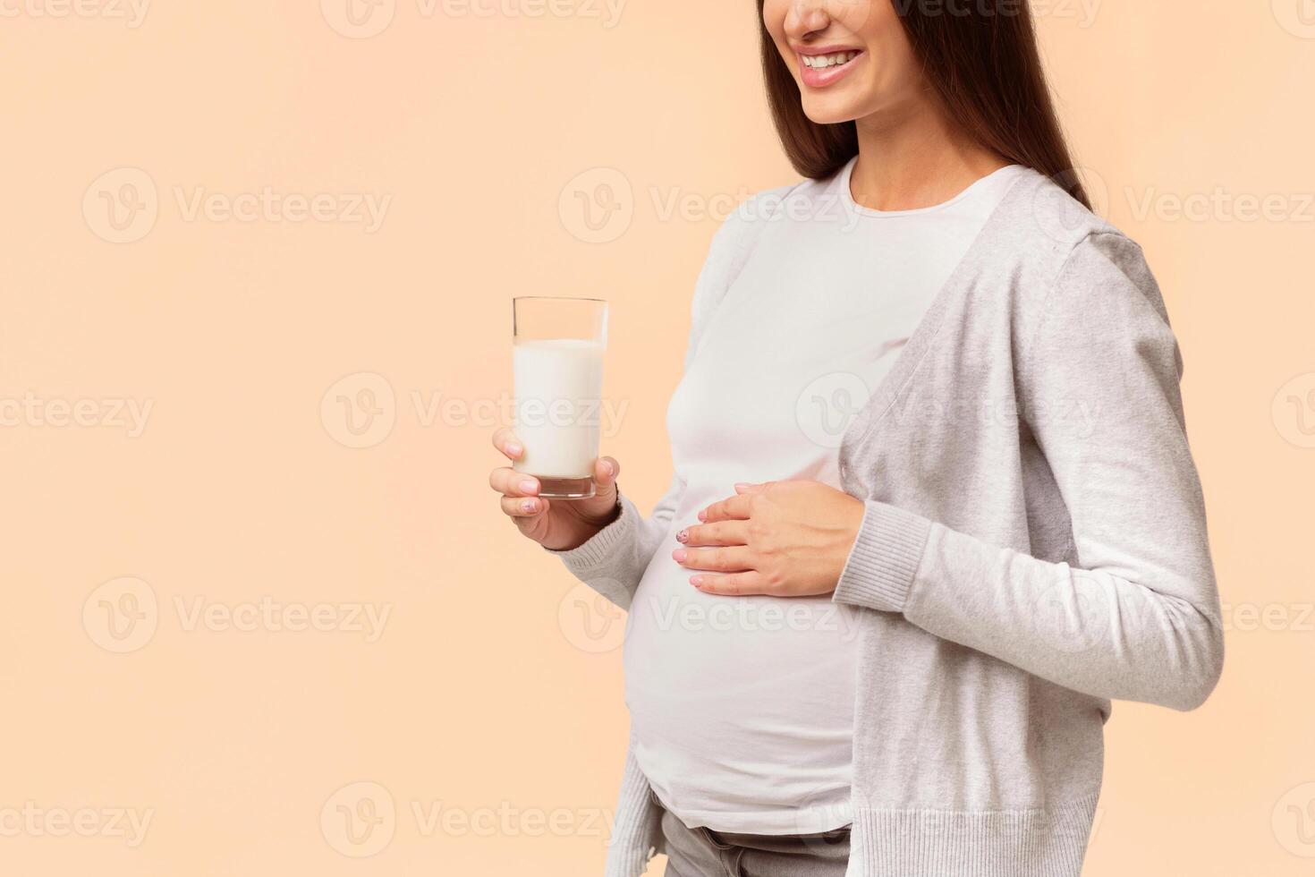 Pregnancy And Healthy Diet. Pregnant Lady Holding Glass Of Milk Standing Over White Studio Background. Cropped, Copy Space photo