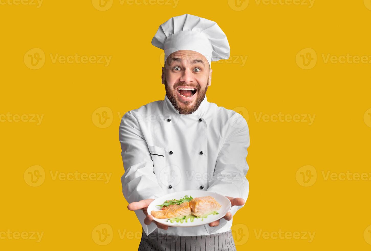 Excited Chef Man Showing Plate Serving Salmon Fish Dish Posing On Black Background. Studio Shot photo